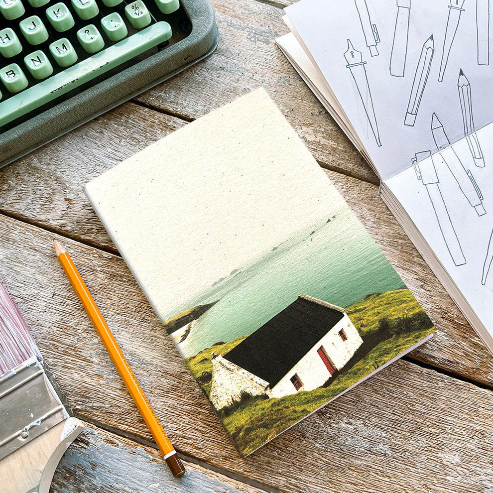 A notebook with a photograph of a white house on the cover, placed on a wooden table alongside a typewriter and pencils.