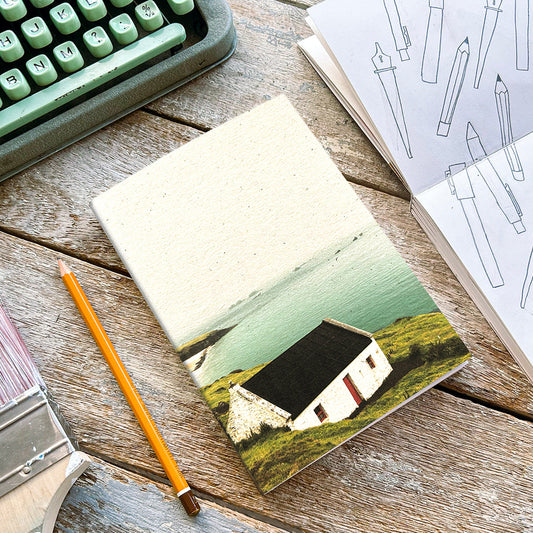A notebook with a photograph of a white house on the cover, placed on a wooden table alongside a typewriter and pencils.