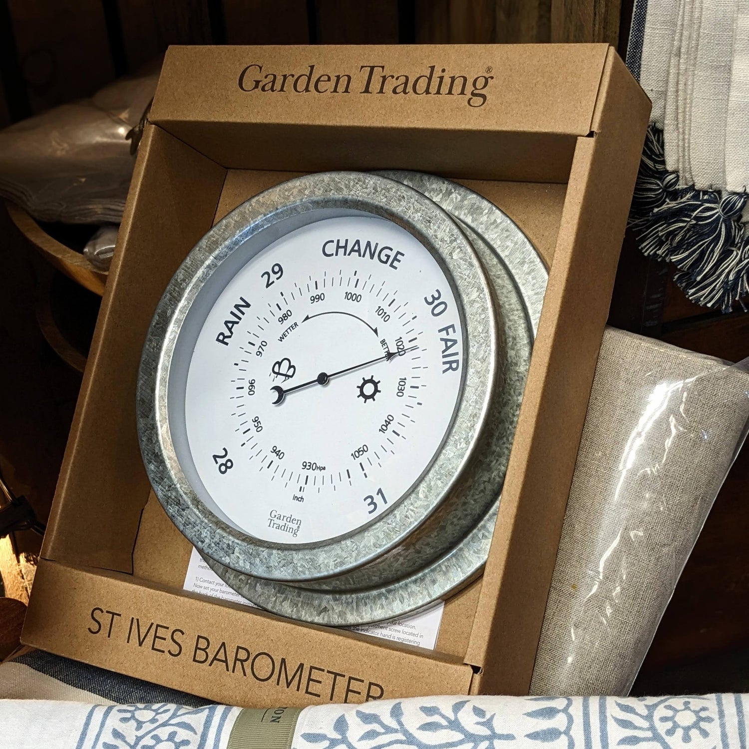A silver analog wall-mounted barometer in a cardboard box with the label 'GARDEN TRADING St Ives Barometer' on top.