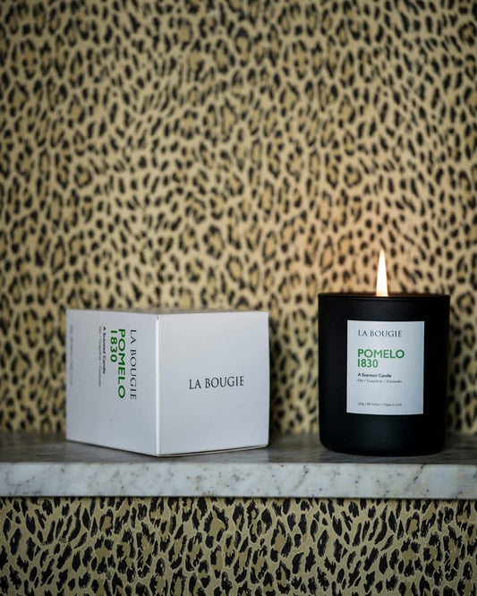 A black candle with a lit flame, next to a white box with 'LA BOUGIE' printed on it, against a leopard print background.