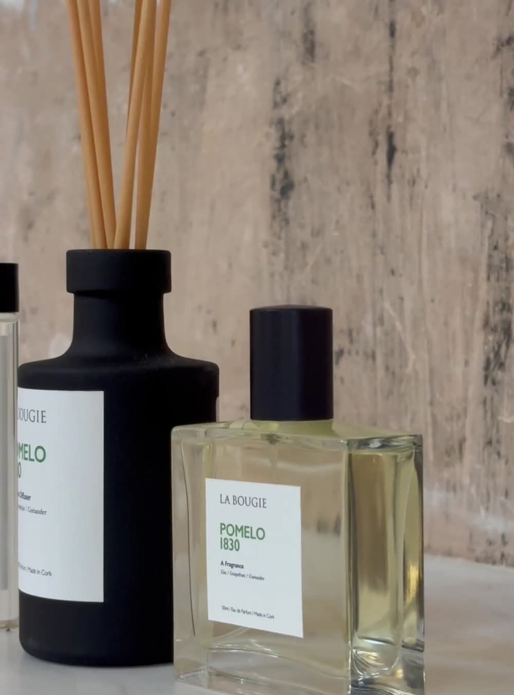 A bottle of POMELO 1830 EAU DE PARFUM 50ML with a clear liquid visible inside, accompanied by a black diffuser with wooden sticks.
