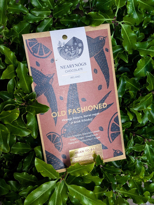 A chocolate bar packaging with 'Old Fashioned Irish' text, depicting orange slices and feathers, placed on a leafy background.