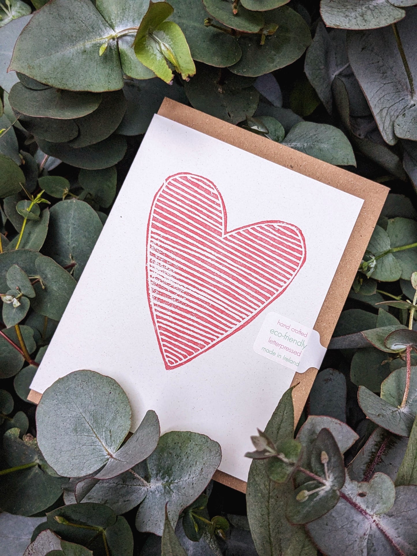 A greeting card with a heart design, made from tree-free cardstock, positioned on a bed of green leaves.